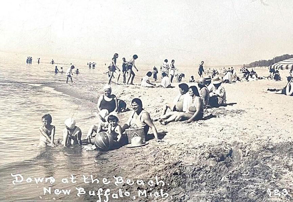 antique photo of people sitting at the new buffalo beach near the water