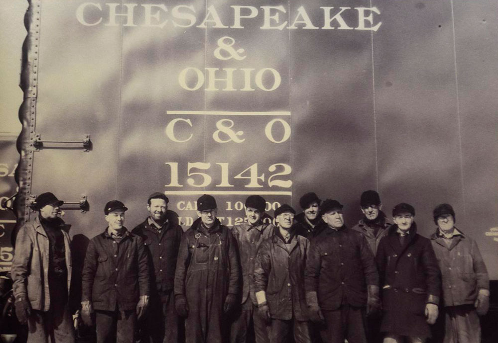 vintage photo of a group of men in working clothes posing in front of a train car